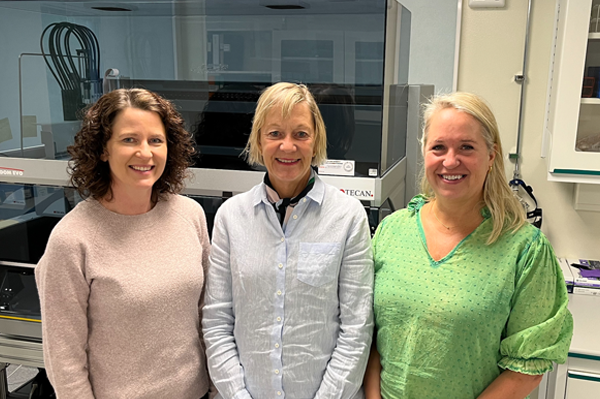 Three smiling white women stand in a laboratory setting