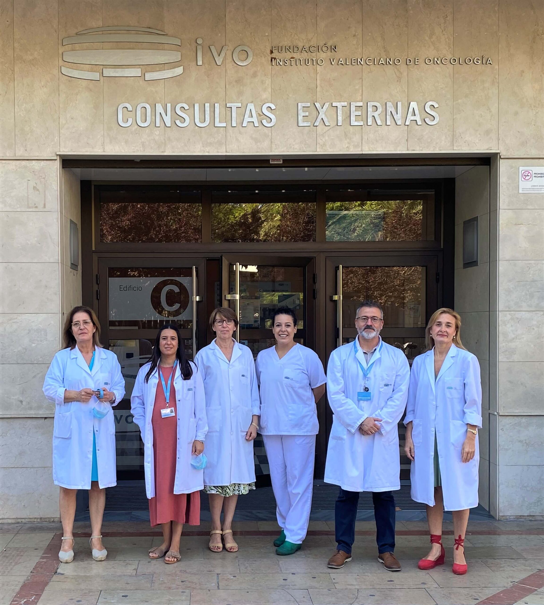 a group of bio bankers wear white coats and stand in front of a hospital entrance