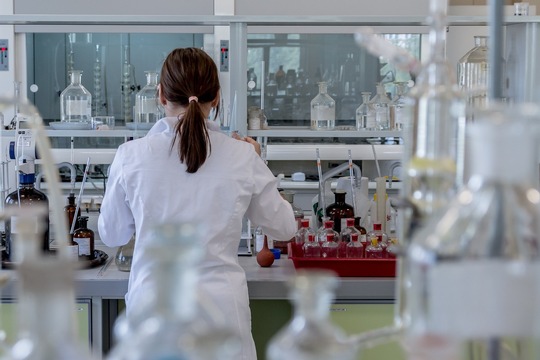photo of a woman with hair in a ponytail and wearing a white lab coat working in a laboratory