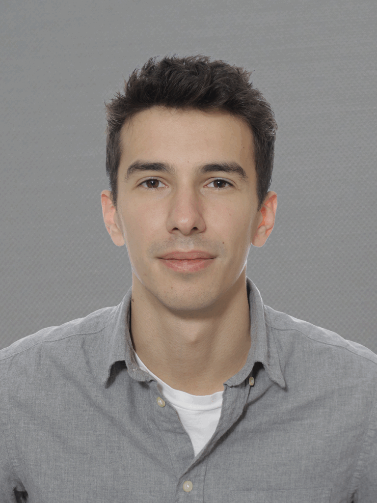 portrait of a white man with short textured dark hair. He is wearing a grey shirt